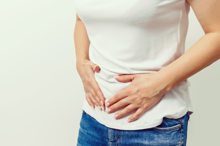 Mulher tocando a mão na barriga com dor - Pop Saúde